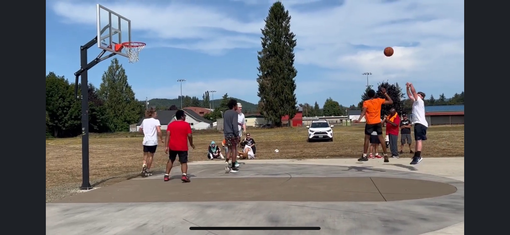 A player with a defender shoots from distance on an outdoor basketball court.